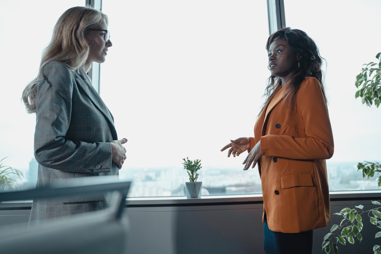 Two professional women in a corporate office having a conversation by the window.
